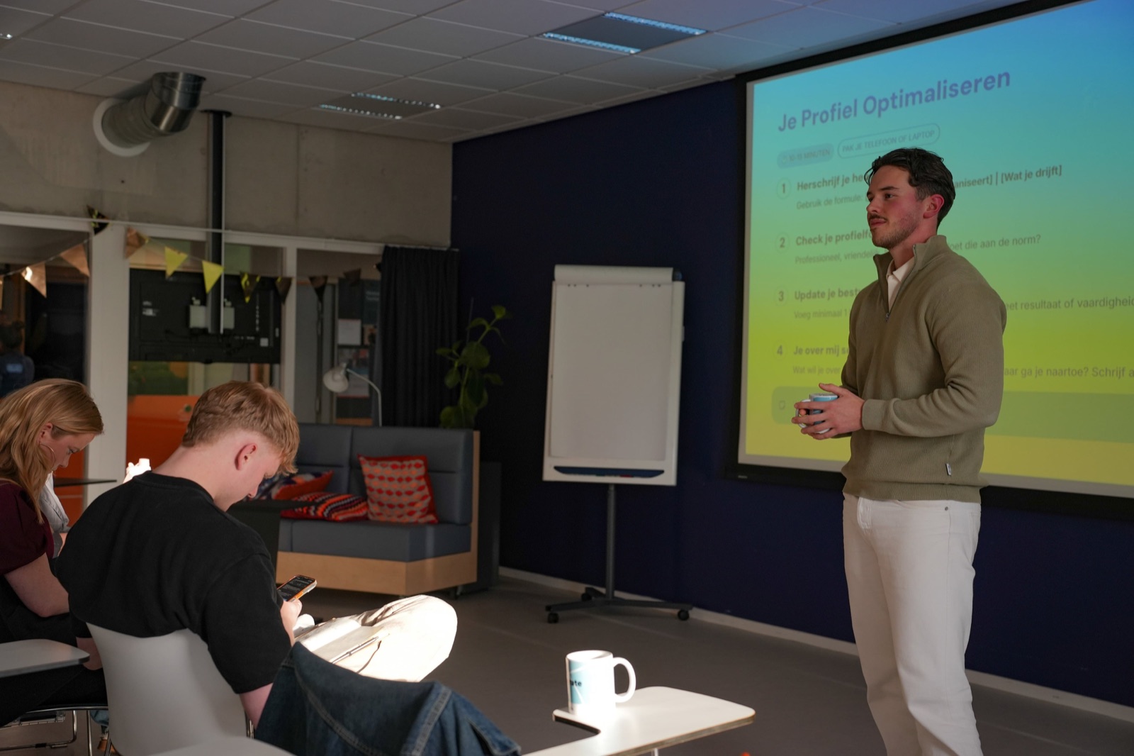 Nick staat naast een scherm en geeft een training aan een groep deelnemers.